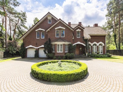 Front view of a driveway with a round garden and big, english style house in the background. Real photo